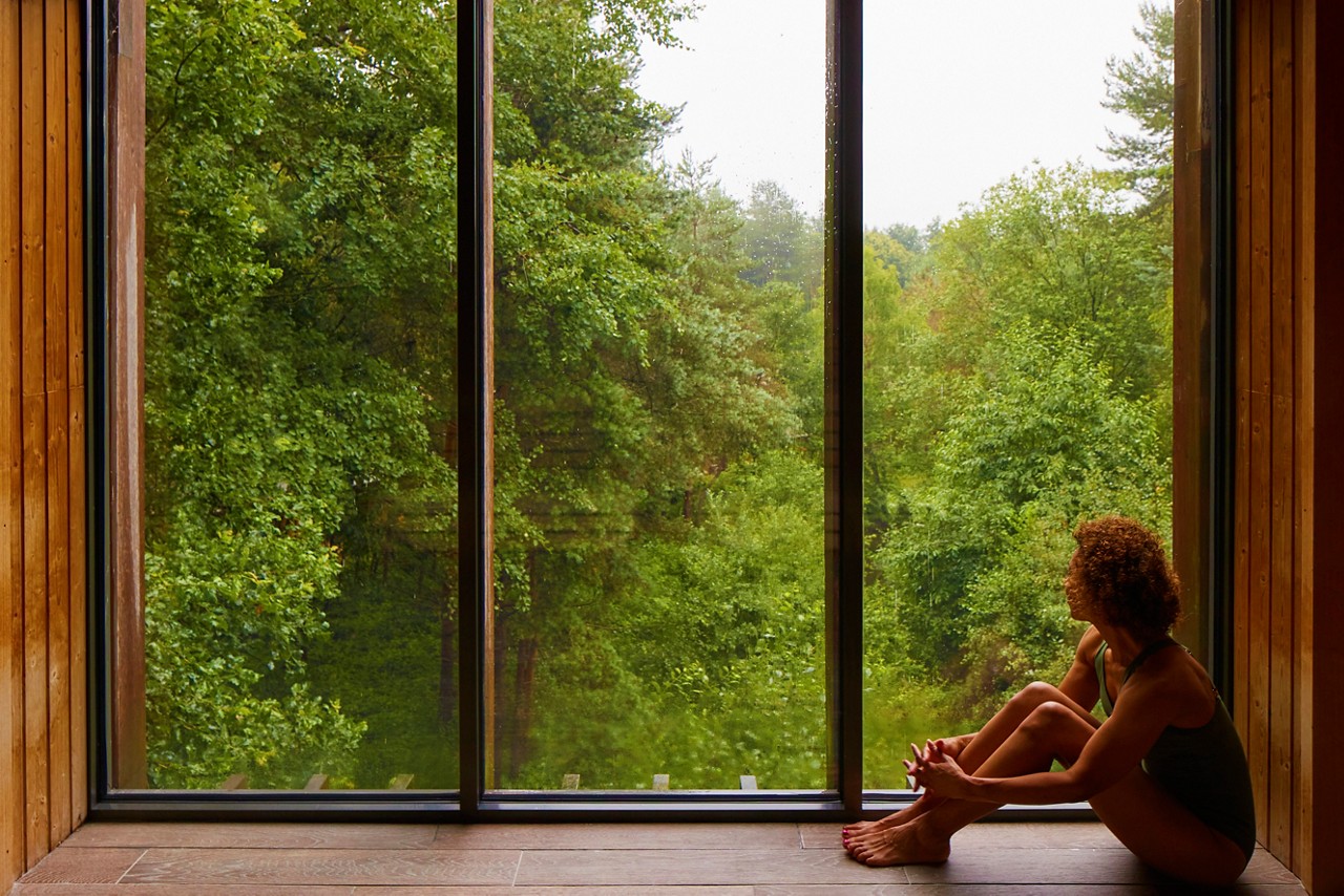 Woman sat looking out at the forest from inside the Treetop Sauna.